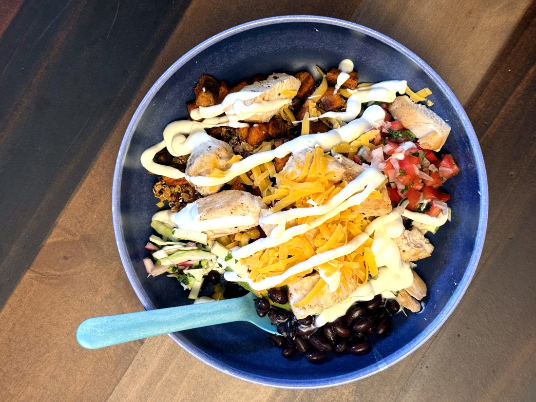 The bowl variation — quinoa, black beans, roasted sweet potato, chicken, avocado, pico de gallo, and lime crema in a blue bowl