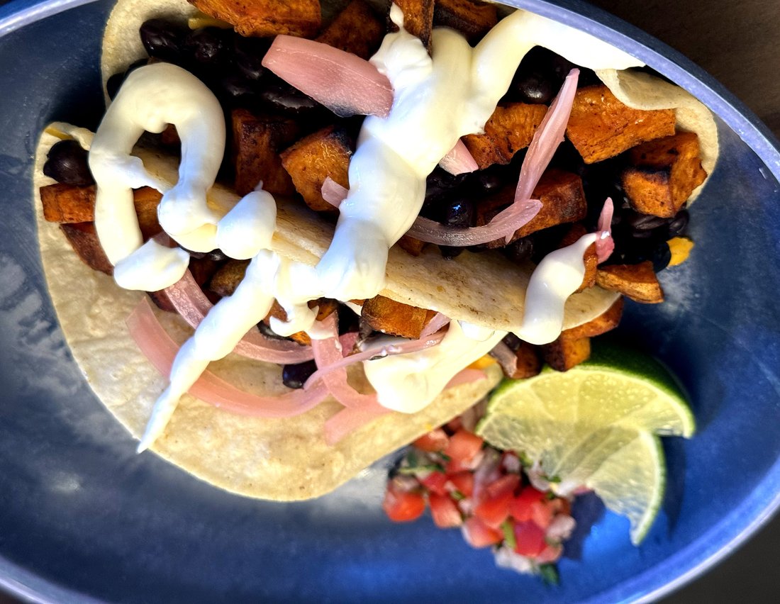 Black bean and sweet potato tacos on corn tortillas — roasted sweet potato, black beans, pickled red onions, and lime crema drizzle, with pico de gallo and lime wedges on a blue plate