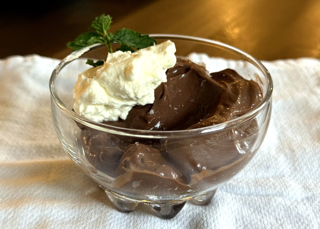 Stovetop chocolate pudding topped with fresh whipped cream and a sprig of mint