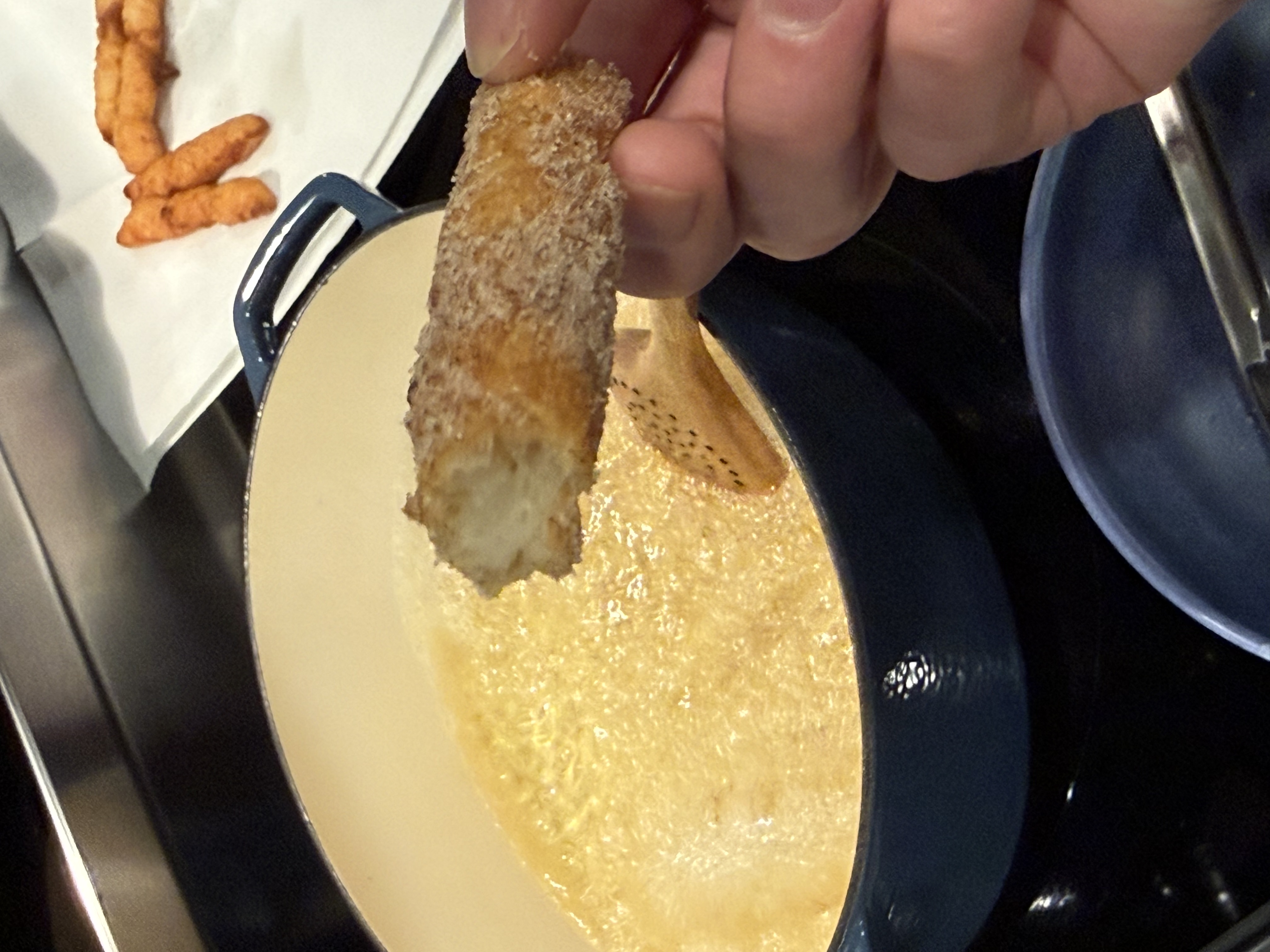 Churro being pulled from hot oil in blue Dutch oven