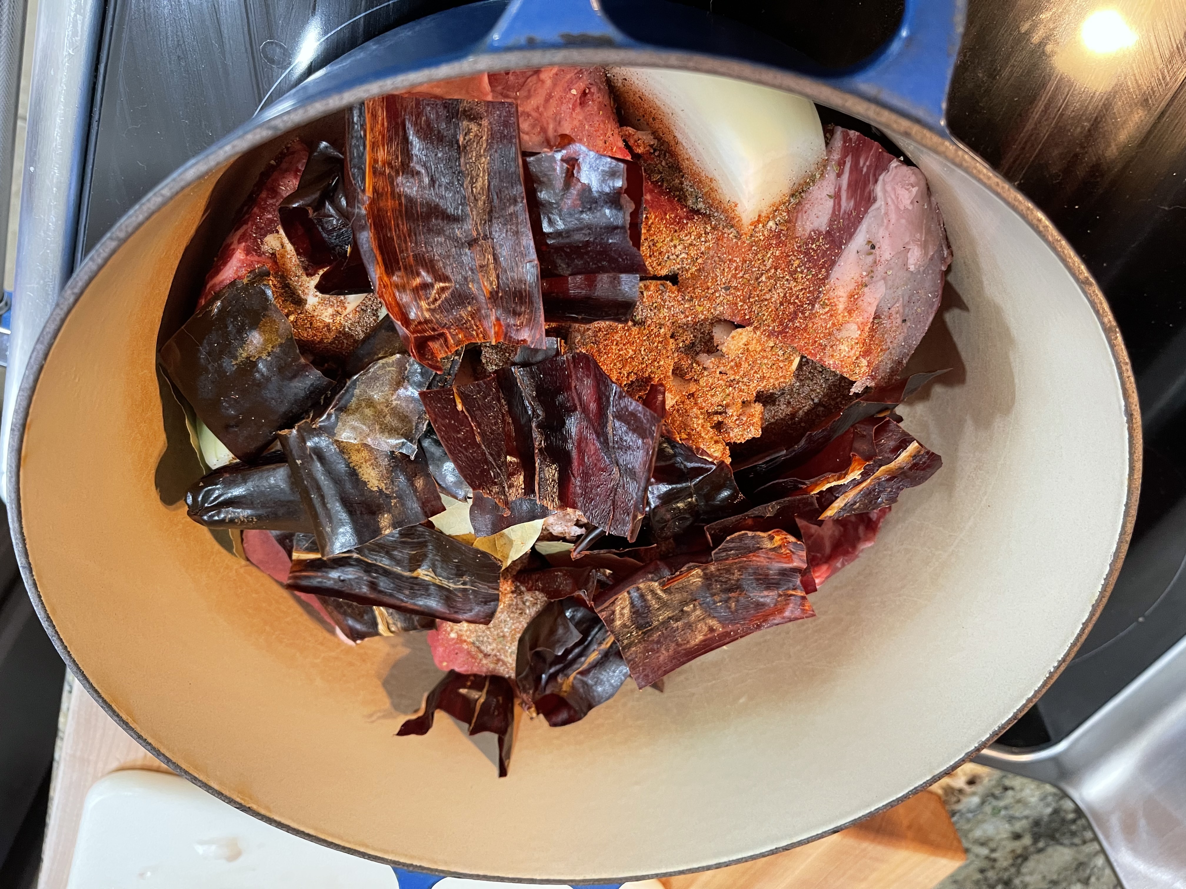 Pork shoulder in a blue Dutch oven with torn dried chiles, chili powder, and onion — ready to braise