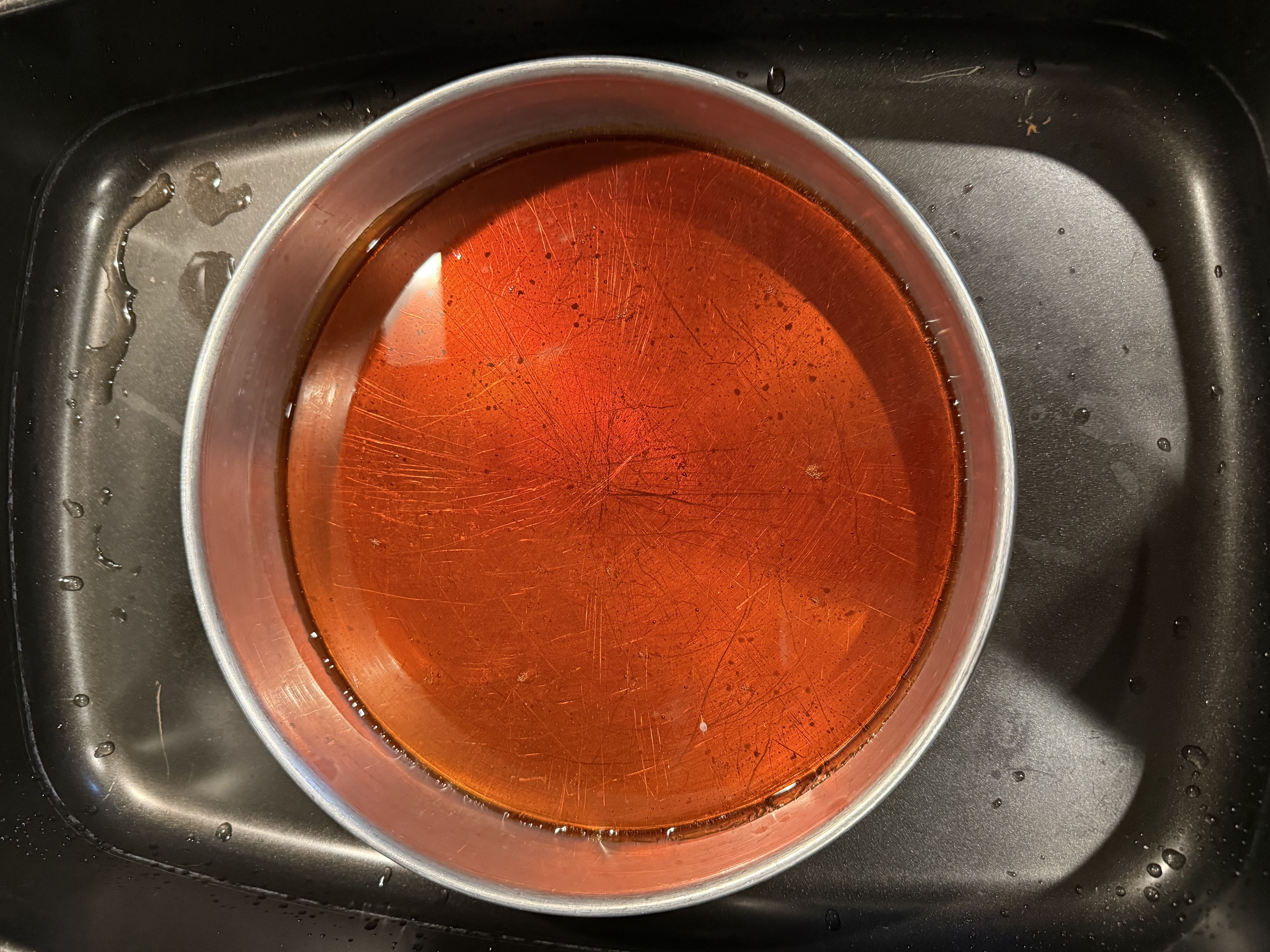 Flan in its baking pan set in a water bath — overhead view of the amber caramel layer before unmolding