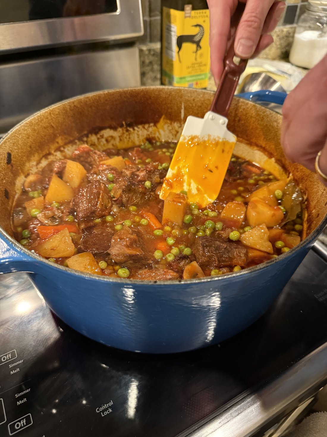 Beef stew being stirred in a blue Dutch oven on the stovetop