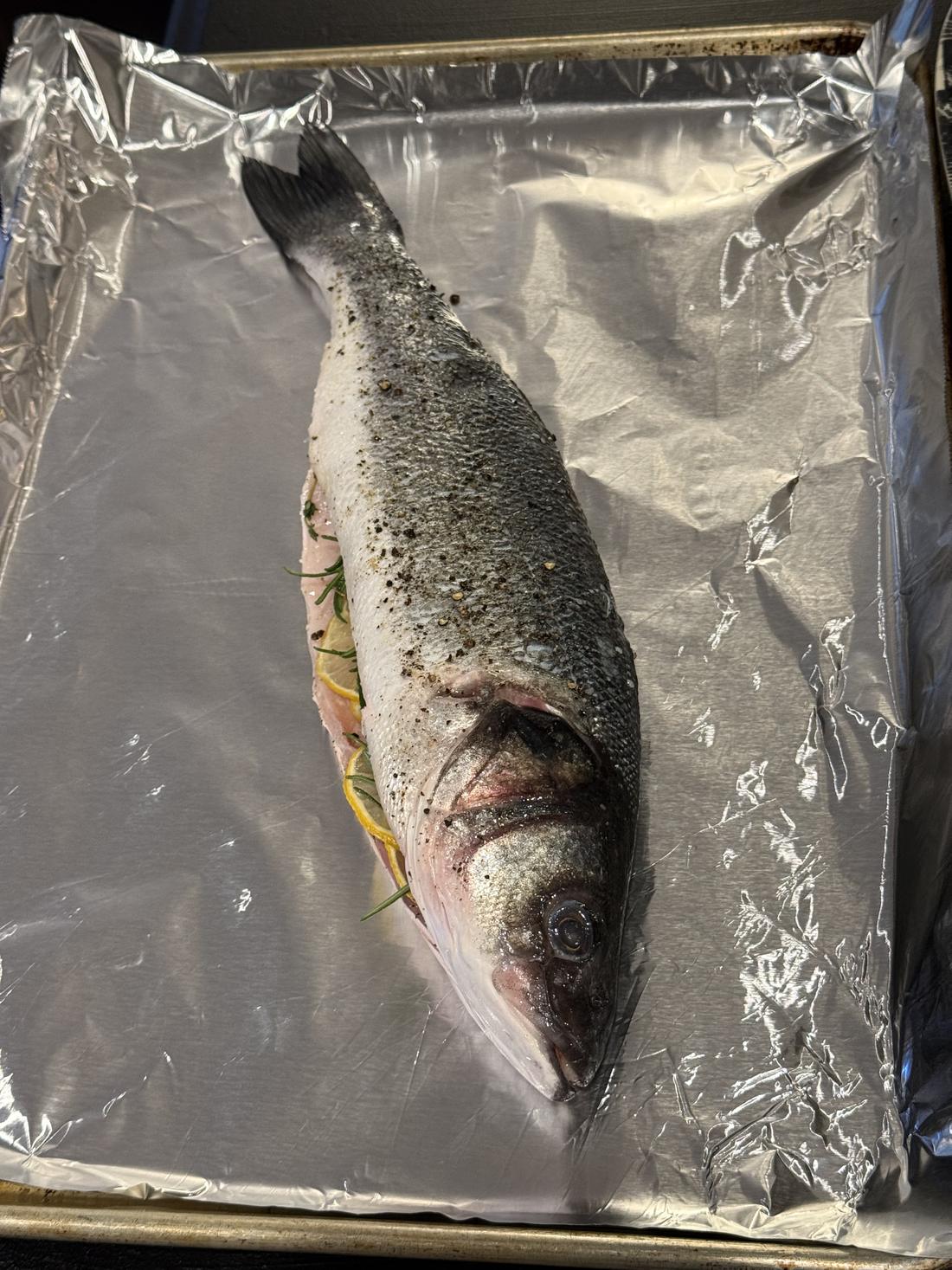 Whole branzino on a foil-lined sheet pan, stuffed with lemon slices and fresh herbs, ready for the oven