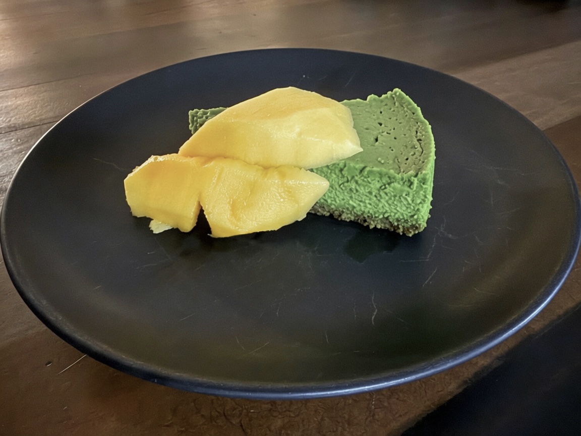 Slice of pale green matcha cheesecake on a graham crust dusted with matcha