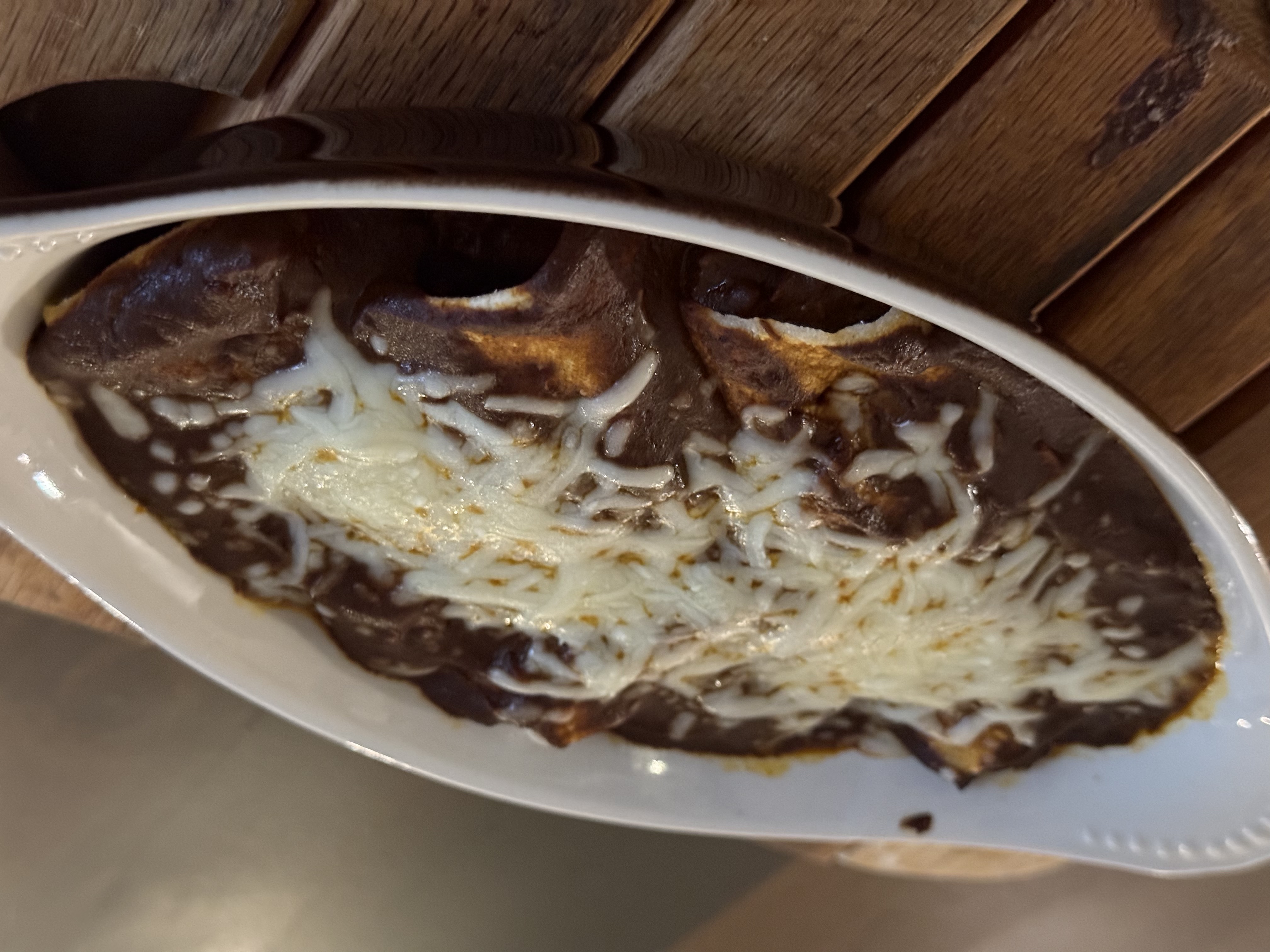 Chicken mole enchiladas in a white oval dish, blanketed in dark mole sauce and melted cheese