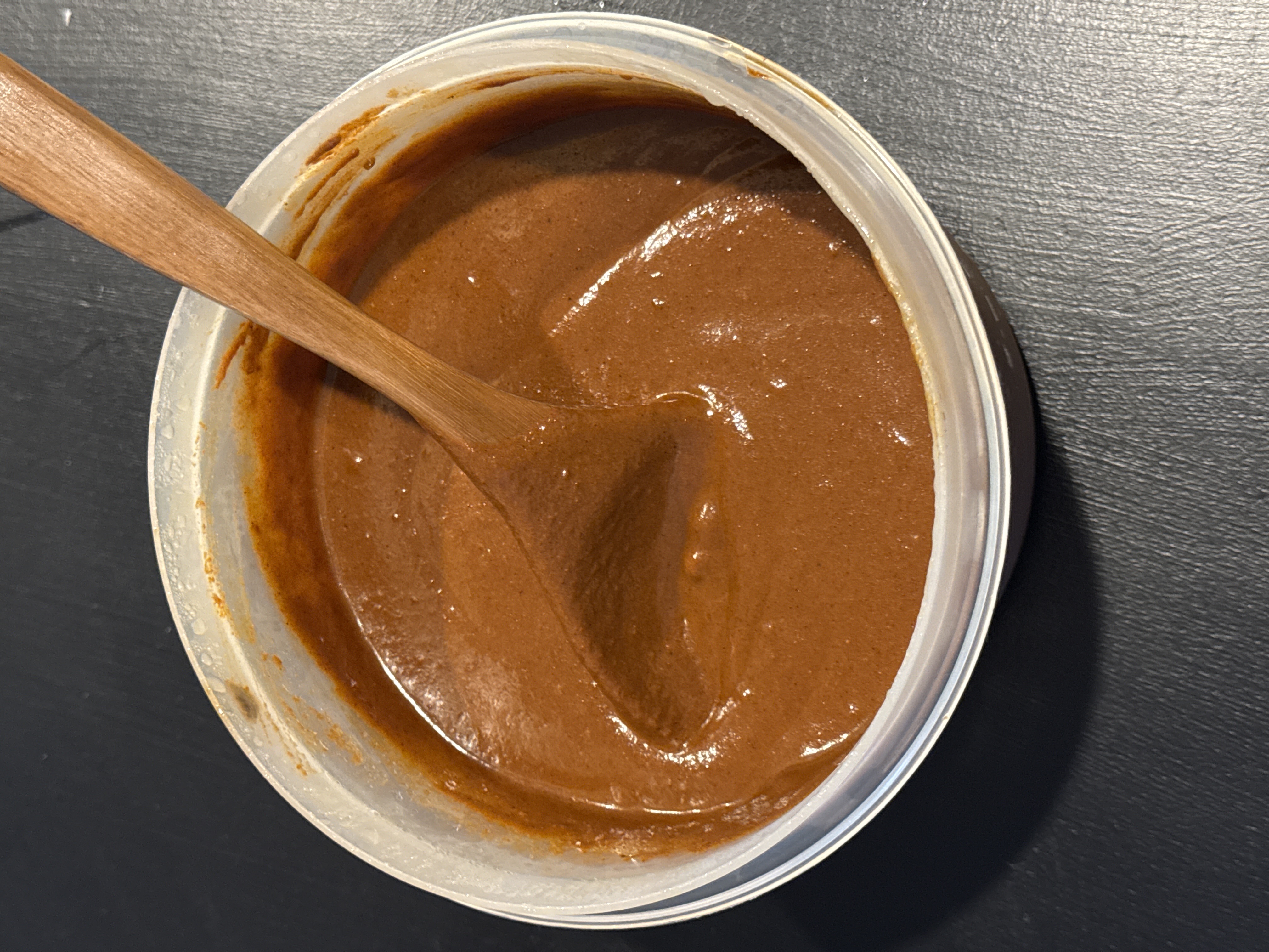 Finished mole negro — smooth dark brown sauce in a container with a wooden spoon