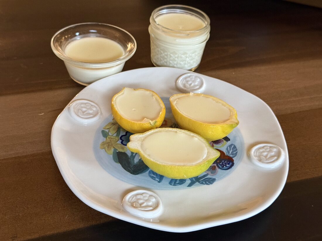 Lemon posset chilled and set in hollowed lemon halves on a floral plate, with two more in a bowl and a jar