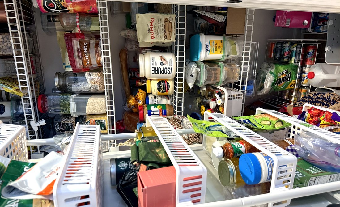 A fully stocked pantry with wire shelving — Rummo pasta, almonds, quinoa, olive oil, and the building blocks of a well-equipped kitchen