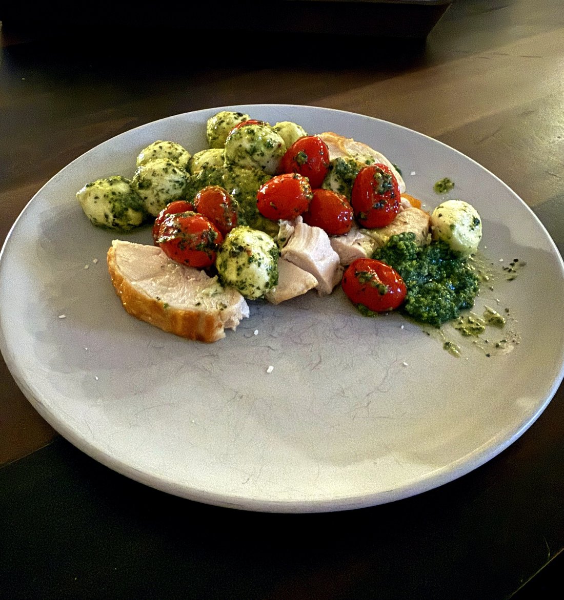 Pesto chicken insalata caprese on a white oval platter — golden pan-roasted chicken slices alongside ciliegine and cherry tomatoes tossed in almond pesto