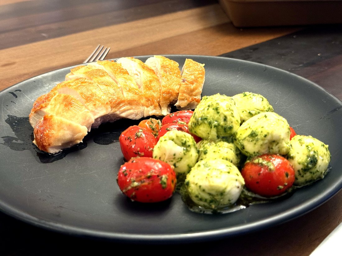 Pesto chicken insalata caprese — pan-seared chicken with almond pesto, ciliegine, and cherry tomatoes on a dark plate