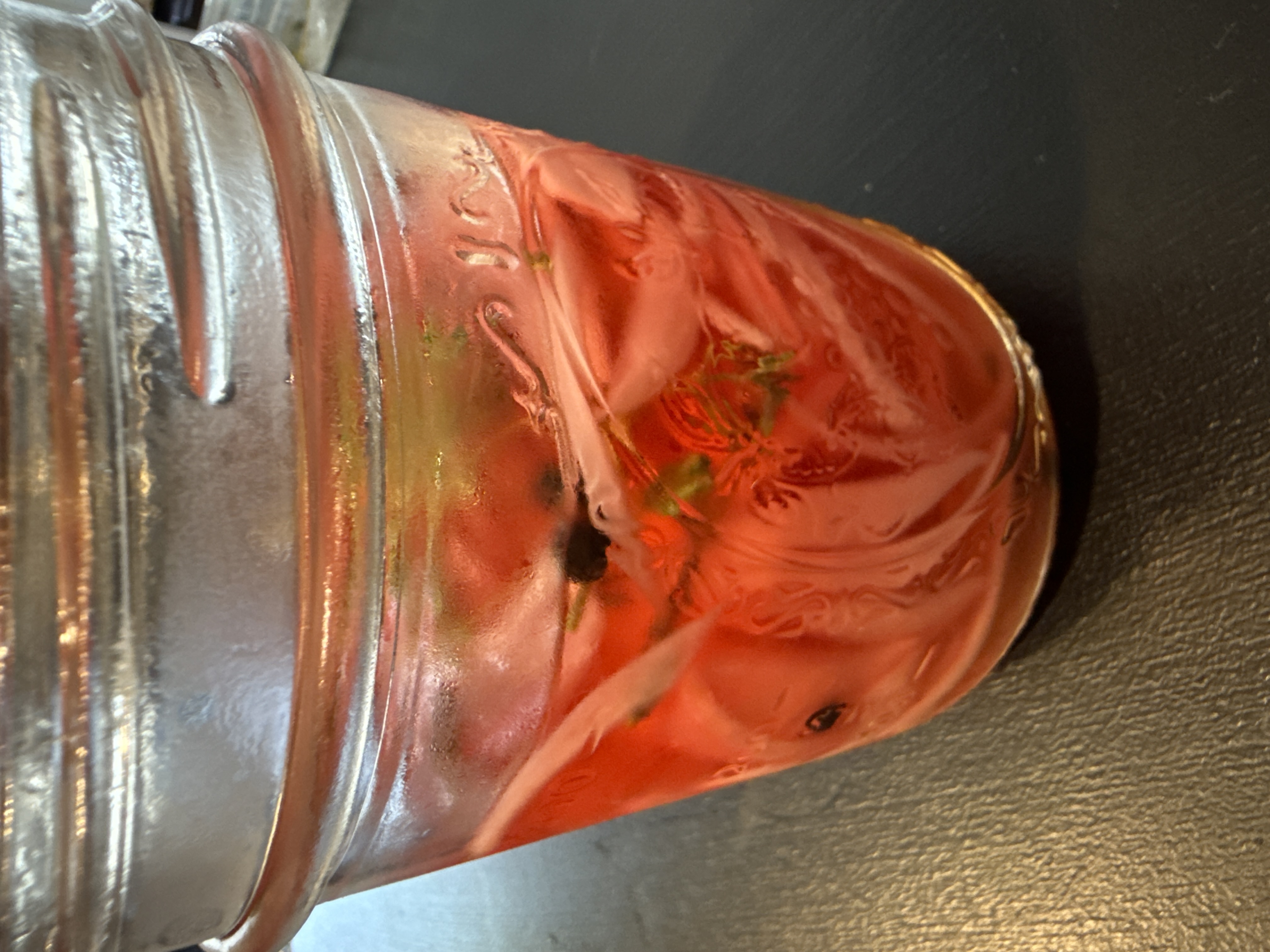 Side view of a mason jar packed with bright pink pickled red onions, thyme, and peppercorns