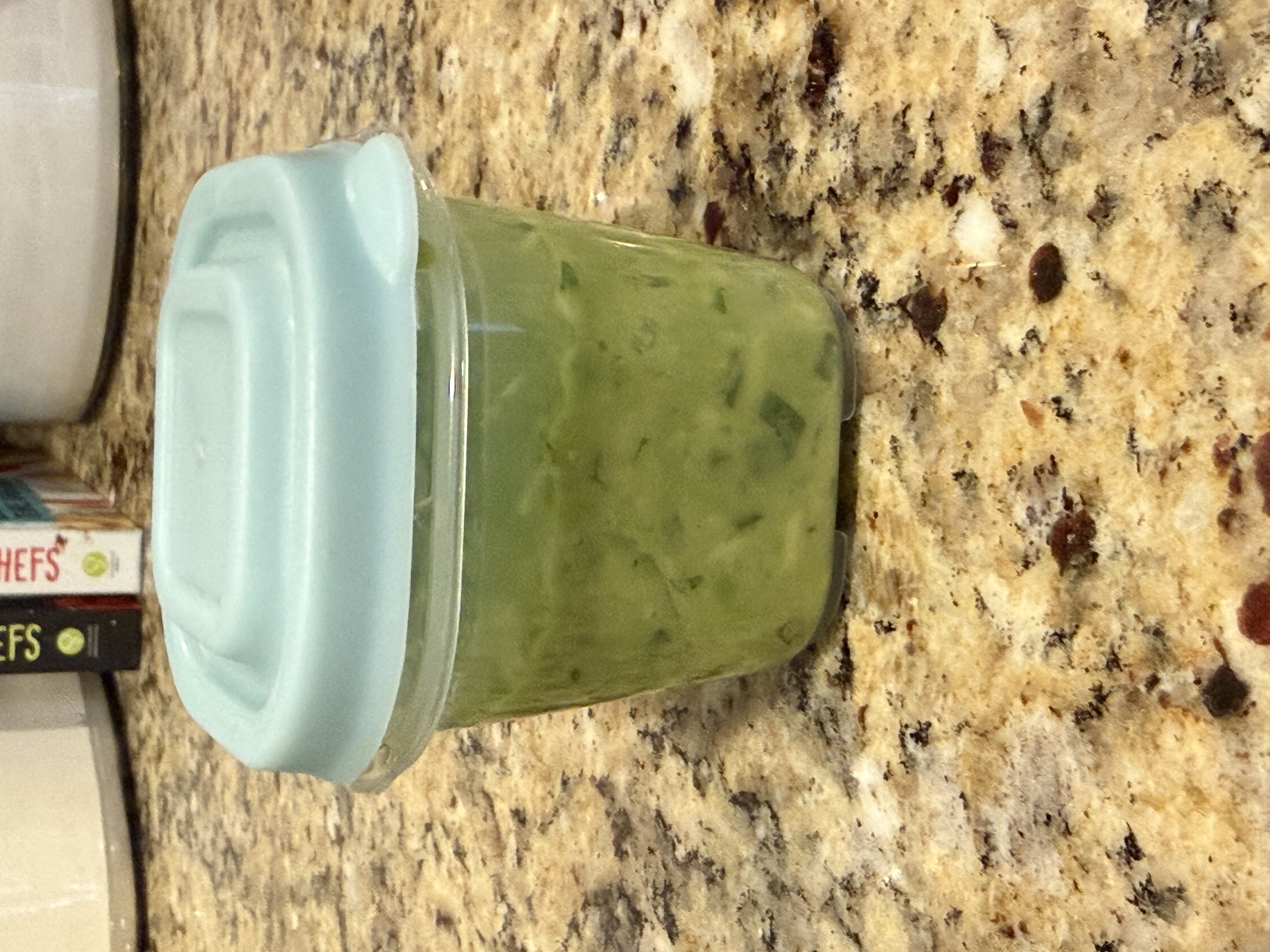 Finished guacamole in a glass container with a teal lid