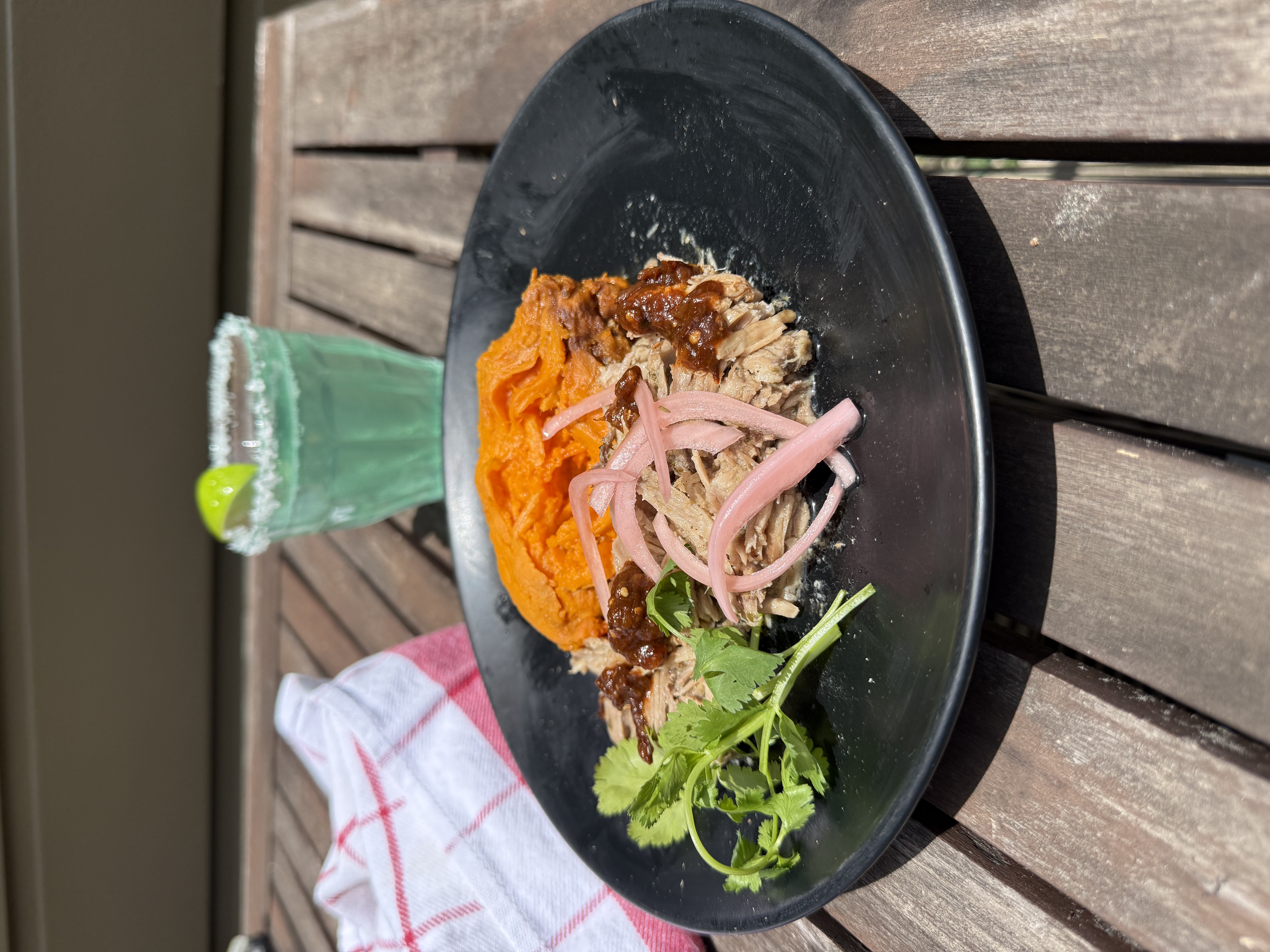 Carnitas bowl — mashed sweet potato, roasted chile salsa-drizzled pulled pork, pickled red onions, and cilantro in a dark bowl