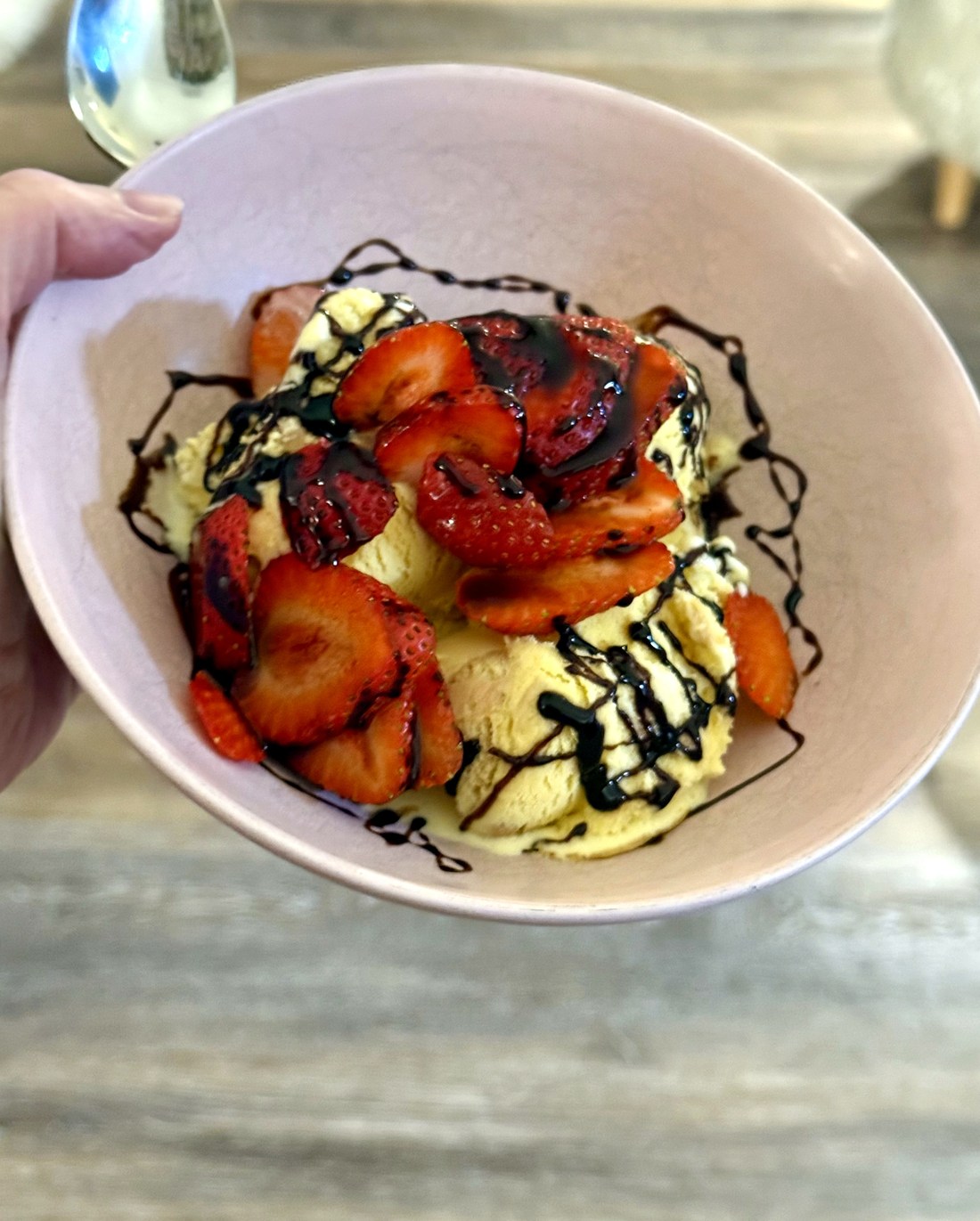 Macerated strawberries and balsamic glaze spooned over vanilla gelato in a pink bowl