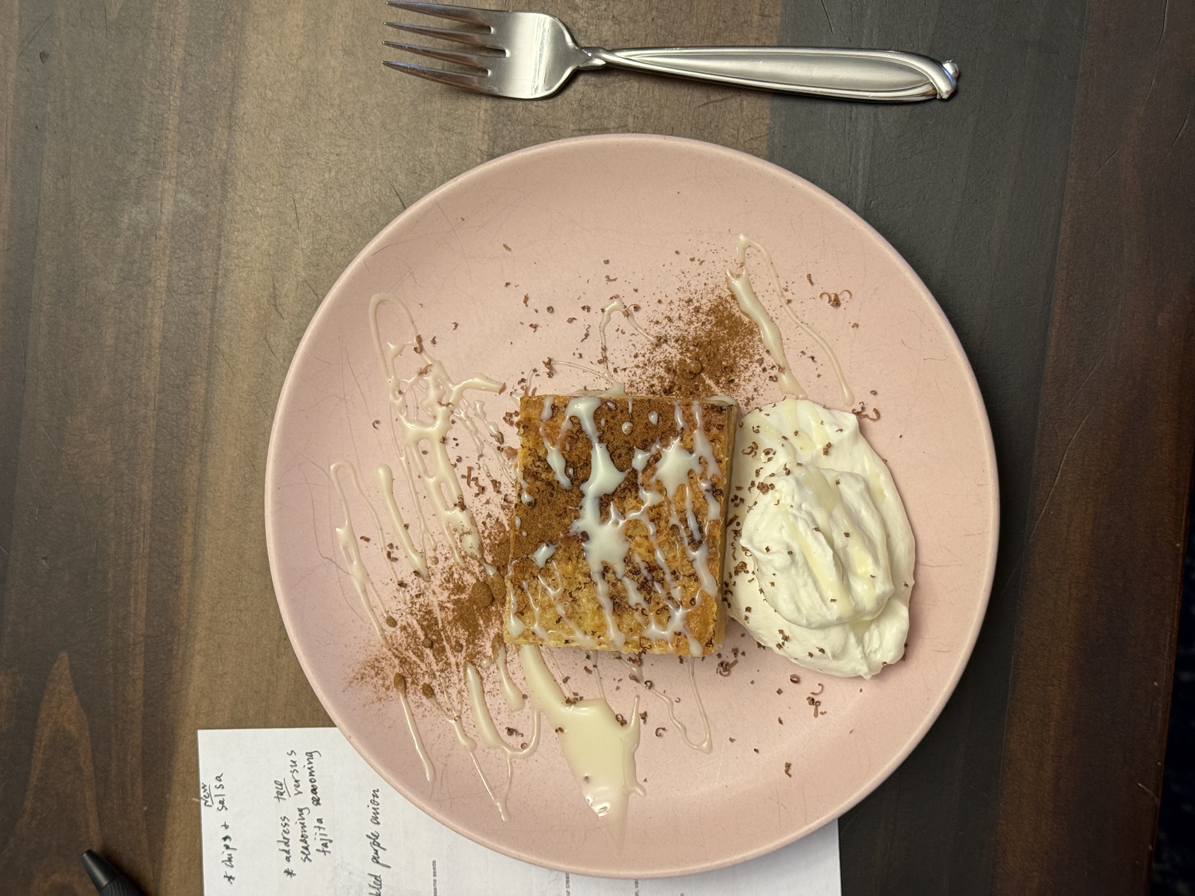 Plated slice of tres leches bread pudding with cream drizzle and cinnamon on a pink plate