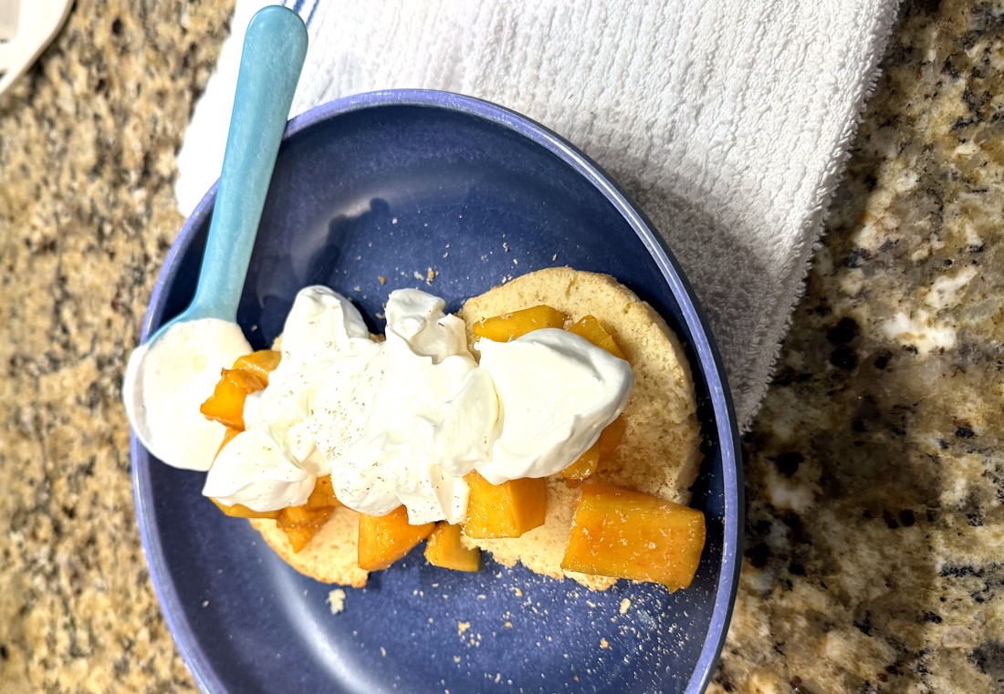 Macerated peaches and whipped cream piled onto a split shortcake biscuit on a blue plate
